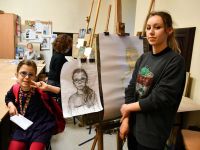 Dziewczynka pozuje do portretu rysowanego przez uczestniczkę zajęć malarstwa